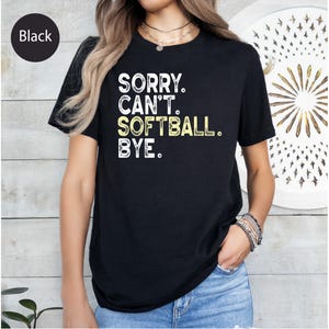 May include: Black t-shirt featuring the text "SORRY. CAN'T. SOFTBALL. BYE." in white and yellow. The shirt has a crew neck.