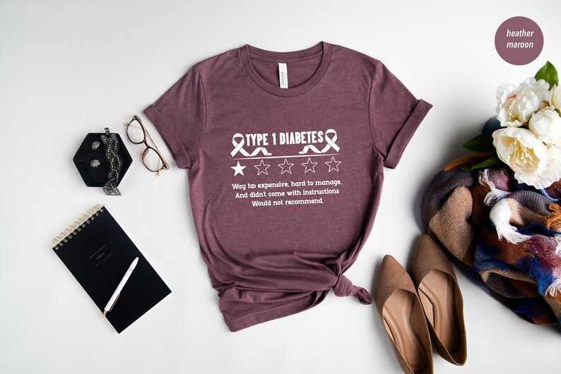 K&ouml;nnte beinhalten: Ein T-Shirt in Heidelbeer-Maroon mit einer wei&szlig;en Grafik eines Bandes und dem Text "TYPE 1 DIABETES" mit einer Ein-Sterne-Bewertung und dem Text "Way too expensive, hard to manage, And didn't come with instructions Would not recommend."