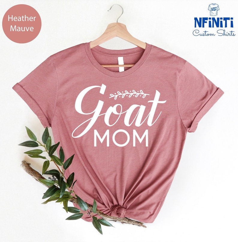 May include: Heather mauve t-shirt with the text "Goat Mom" in white lettering with a small leafy design above the word "Goat".