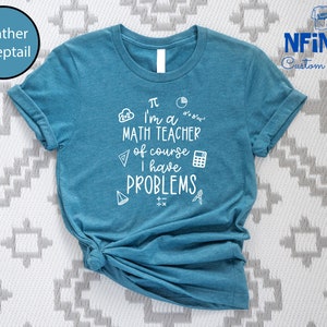 May include: A teal blue t-shirt with white text that reads "&pi; I'm a MATH TEACHER of course I have PROBLEMS". The text is surrounded by math symbols like a calculator, a compass, and a triangle.
