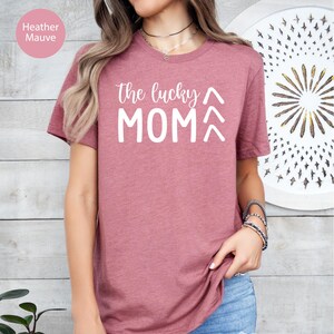 May include: Heather mauve t-shirt with the text "the lucky MOM" in white. The shirt has short sleeves and a crew neck. The text is in a handwritten style font.