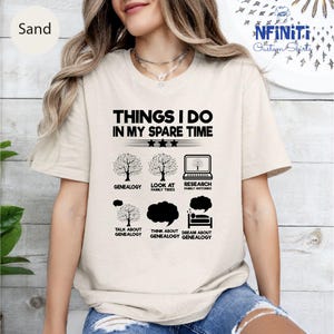 May include: Sand-colored t-shirt with the text "THINGS I DO IN MY SPARE TIME" and graphics related to genealogy. The graphics include trees, a laptop, and speech bubbles. The shirt is a casual wear item.