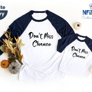 May include: Two white and navy blue baseball shirts with the text "Don't Miss Chance" in black. The shirts are on a white surface with fall leaves and pumpkins.