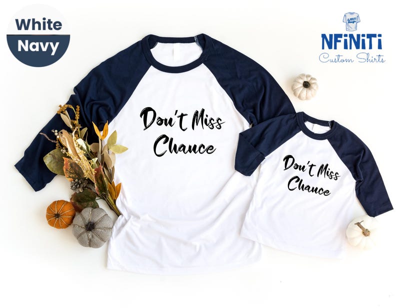 May include: Two white and navy blue baseball shirts with the text "Don't Miss Chance" in black. The shirts are on a white surface with fall leaves and pumpkins.