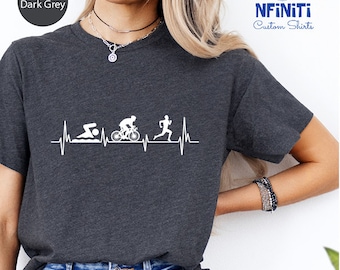 May include: Heather dark grey t-shirt with a white graphic of a heartbeat with a swimmer, cyclist, and runner. The text "NFINITI Custom Shirts" is in the top right corner of the image.