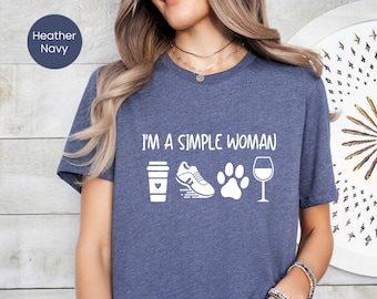 May include: Heather navy blue t-shirt with the text "I'm a simple woman" and four white icons: a coffee cup with a heart, a running shoe, a paw print, and a wine glass.