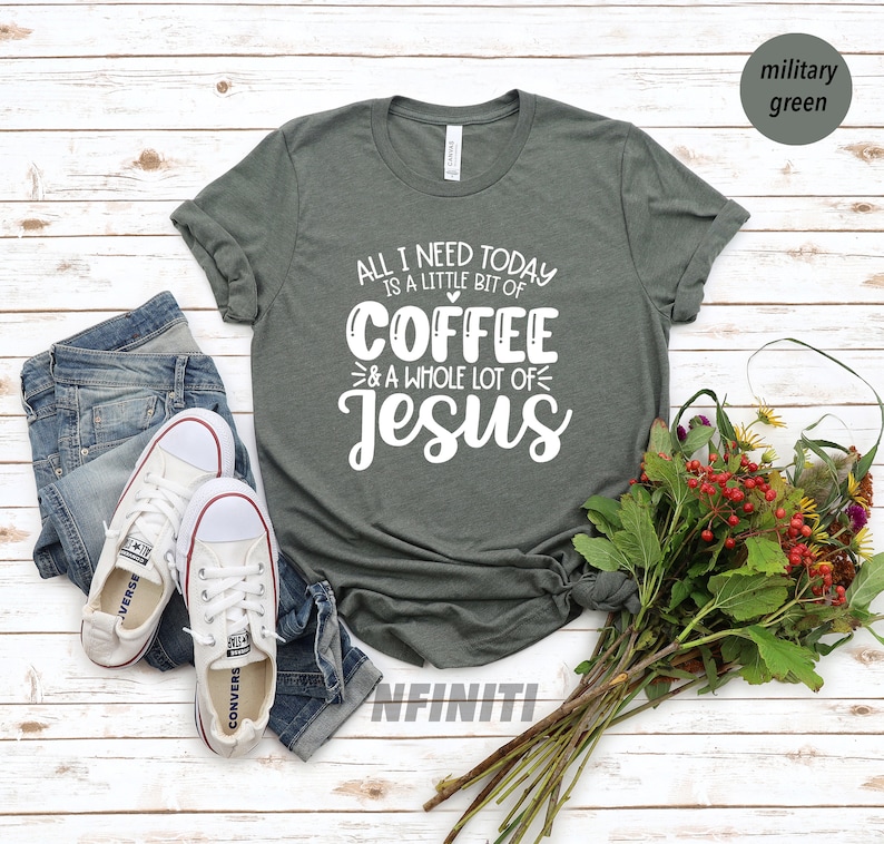 May include: Military green t-shirt with the text "All I need today is a little bit of coffee & a whole lot of Jesus" in white. The shirt is paired with blue jeans and white canvas sneakers. A bouquet of flowers rests on the side.