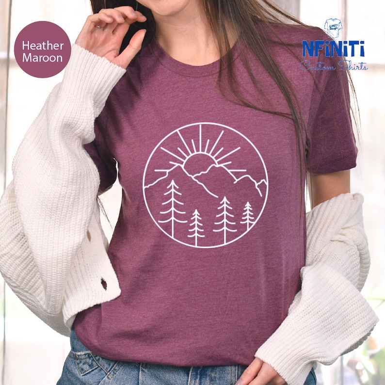 a woman wearing a maroon shirt with a mountain scene on it