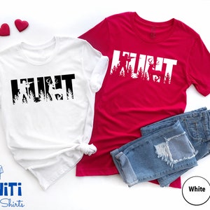May include: Two t-shirts with the word "HUNT" in black and white, with a silhouette of a hunter and deer inside the letters. The shirts are on a white background with blue jeans and red hearts.