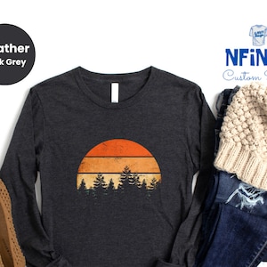 May include: A heather dark grey long-sleeve t-shirt with a vintage sunset graphic featuring a line of trees. The text "NFINITI Custom Shirts" is visible in the top right corner of the image.