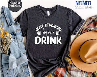 May include: A dark heather grey t-shirt with the text "JUST DIVORCED buy me a DRINK" in white. The text is surrounded by two beer mug icons.
