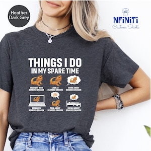 Peut inclure: Un t-shirt gris foncé chiné avec le texte "Things I do in my spare time" et des illustrations de dragons barbus. Les illustrations montrent un dragon barbu en train d'être tenu, regardé, pensé, recherché, discuté et rêvé.