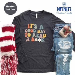 May include: A dark grey long-sleeved t-shirt with the text "IT'S A GOOD DAY TO READ A BOOK" in colorful retro lettering with a daisy graphic.