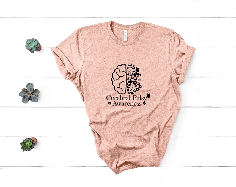 Może przedstawiać: Jasnor&oacute;żowy t-shirt z czarnym konturem m&oacute;zgu z kwiatami i motylami po jednej stronie i tekstem "Cerebral Palsy Awareness" po drugiej.