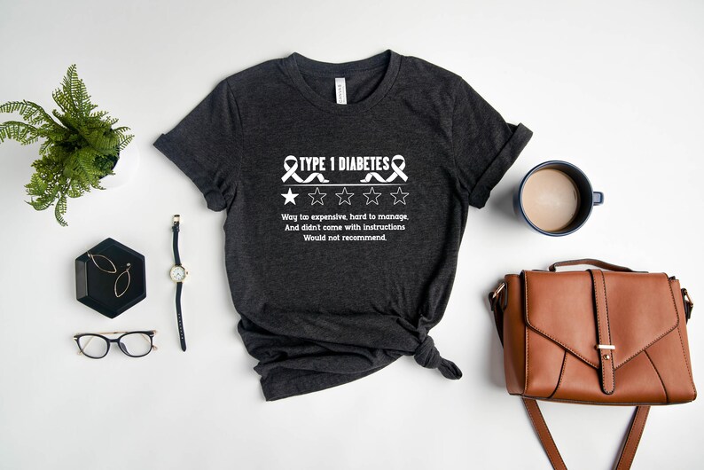 K&ouml;nnte beinhalten: Ein dunkelgraues T-Shirt mit einem wei&szlig;en Band und dem Text "TYPE 1 DIABETES" und einer Ein-Sterne-Bewertung. Der Text unter der Bewertung lautet "Way too expensive, hard to manage. And didn't come with instructions. Would not recommend."