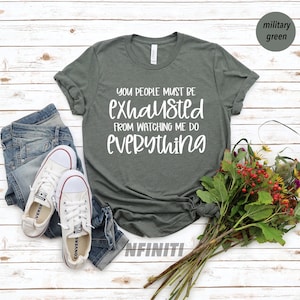 May include: A dark green t-shirt with white text that reads "You people must be exhausted from watching me do everything".