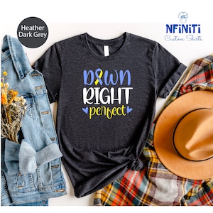 Op de afbeelding: Heather donkergrijs T-shirt met de tekst "Down Right Perfect" en een geel en blauw lint. Het shirt ligt op een geruite deken met een bruine hoed.