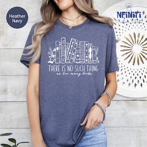 May include: Heather navy t-shirt with a white graphic of stacked books and the text "THERE IS NO SUCH THING as too many books." The shirt has short sleeves and a crew neck. The shirt is made of a soft, comfortable material.