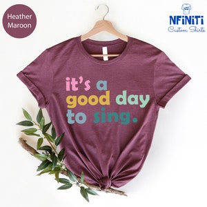 May include: Heather maroon t-shirt with the text "it's a good day to sing." in colorful letters.