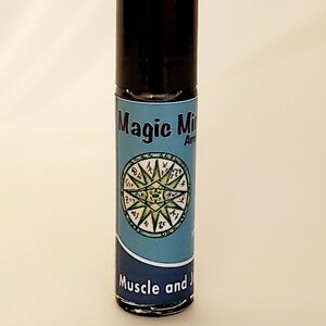 Könnte beinhalten: Eine kleine, schwarze Roll-on-Flasche mit einem blauen Etikett. Das Etikett lautet "Magic Mix" und "Muskel und Gelenk" mit einem grünen und weißen kreisförmigen Design in der Mitte.