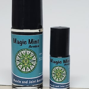 May include: Two roll-on bottles of Magic Mint Arnica Muscle and Joint Anti-Inflammatory oil. The bottles are black with silver caps and feature a green and blue label with a compass design. The larger bottle is 30 ml.