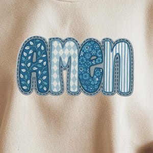 Op de afbeelding: Crèmekleurige sweatshirt met het woord "amen" in blauwe, decoratieve letters. De letters hebben verschillende patronen, waaronder bloemen-, ruit- en streepontwerpen. De sweatshirt is een casual, comfortabele stijl.
