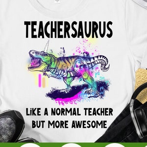 May include: White t-shirt with a colorful dinosaur graphic and the text "TEACHERSAURUS LIKE A NORMAL TEACHER BUT MORE AWESOME".