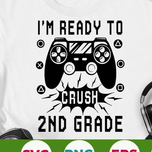 Peut inclure: Un t-shirt blanc avec un graphique noir d'une manette de jeu vidéo et le texte "I'm Ready To Crush 2nd Grade". Le texte est dans une police de caractères pixélisée.