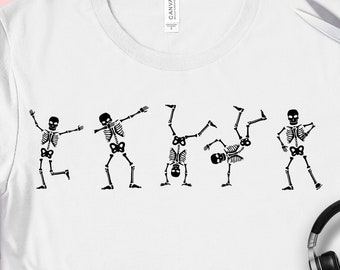 以下が含まれることがあります： 様々なダンスポーズの黒いスケルトンデザインが施された白いTシャツ。スケルトンは遊び心がありダイナミックな方法で描かれています。シャツには「SVG PNG EPS DXF」の文字も入っています。