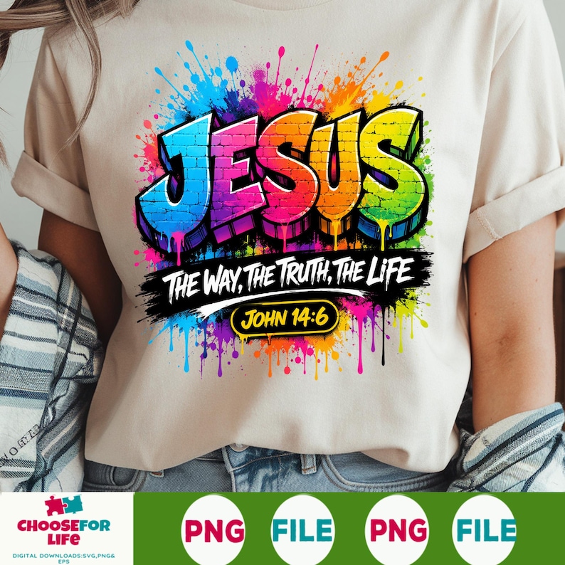 May include: A beige t-shirt featuring a colorful graphic with the word JESUS in a brick-patterned font, surrounded by paint splatters. Below, the text reads THE WAY, THE TRUTH, THE LIFE and JOHN 14:6 in a black brushstroke design with yellow accents.