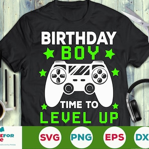 Könnte beinhalten: Ein schwarzes T-Shirt mit einem grün-weißen Design. Das Design zeigt einen Videospiel-Controller mit dem Text "Birthday Boy" und "Time to Level Up".