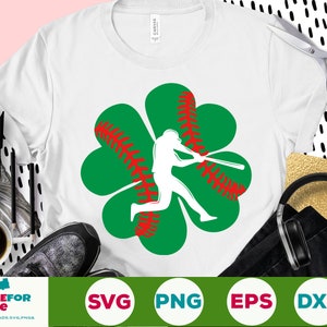 May include: A white t-shirt with a green four-leaf clover design. The clover has a red baseball stitch pattern and a silhouette of a baseball player swinging a bat.