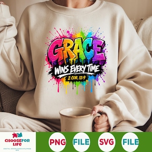 May include: A beige crewneck sweatshirt featuring a vibrant, multi-colored graffiti-style graphic that reads GRACE WINS EVERY TIME 2 COR. 12:9. The design includes bright paint splatters in pink, yellow, blue, and purple surrounding the text.