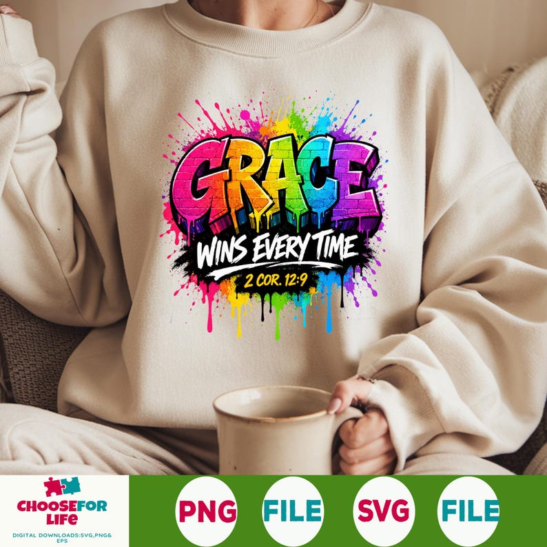 May include: A beige crewneck sweatshirt featuring a vibrant, multi-colored graffiti-style graphic that reads GRACE WINS EVERY TIME 2 COR. 12:9. The design includes bright paint splatters in pink, yellow, blue, and purple surrounding the text.