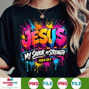 May include: A black t-shirt featuring a colorful graphic with the word JESUS in a brick-like font, followed by the text MY SAVIOR MY STRENGTH and PSALM 28:7. The design includes vibrant paint splatters in pink, blue, yellow, and orange hues.