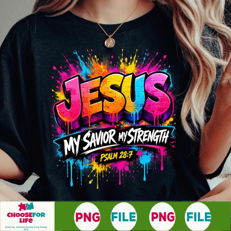 May include: A black t-shirt featuring a colorful graphic with the word JESUS in a brick-like font, followed by the text MY SAVIOR MY STRENGTH and PSALM 28:7. The design includes vibrant paint splatters in pink, blue, yellow, and orange hues.