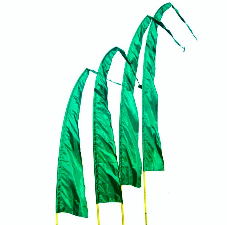 May include: Four green fabric flags with pointed ends are attached to poles and are waving in the wind.
