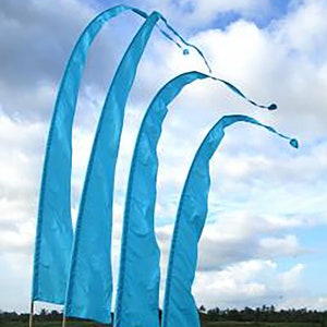May include: Four blue fabric flags with a curved shape, waving in the wind against a blue sky with white clouds. The flags are attached to poles and are displayed outdoors.