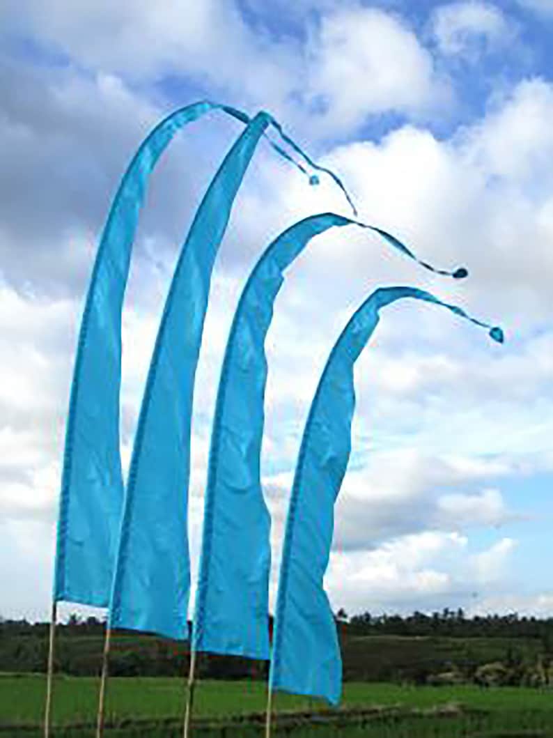 May include: Four blue fabric flags with a curved shape, waving in the wind against a blue sky with white clouds. The flags are attached to poles and are displayed outdoors.