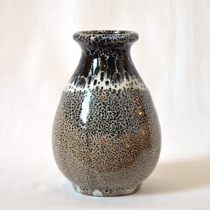 Puede incluir: Un jarrón de cerámica blanco y negro con un esmalte moteado. El jarrón tiene un cuerpo redondo y un cuello estrecho.