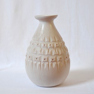 May include: A white ceramic vase with a textured, geometric design. The vase has a rounded body and a narrow neck.
