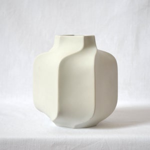 May include: A white ceramic vase with a geometric, faceted design. The vase has a wide, rounded base and a narrow opening.