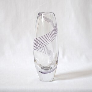 Könnte beinhalten: Eine klare Glasvase mit einem violetten Wirbelmuster. Die Vase ist hoch und schlank mit einem abgerundeten Boden.