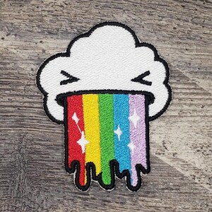 May include: A white cloud with a rainbow coming out of its mouth. The rainbow is dripping and has sparkles on it.