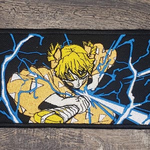 May include: A yellow and blue embroidered patch featuring a character from the anime Demon Slayer. The character is wielding a sword and surrounded by lightning bolts.