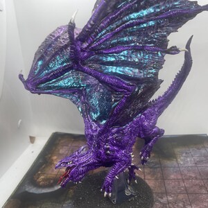 May include: A purple and blue dragon miniature with iridescent wings. The dragon is posed in a flying position with its wings spread wide. The miniature is painted with a detailed, realistic style.