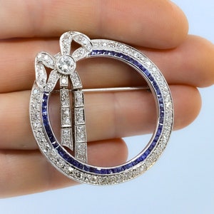 May include: A silver brooch with a diamond bow and a circle of sapphires and diamonds.