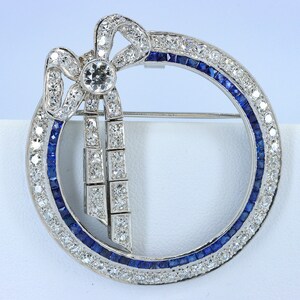 May include: A silver brooch with a diamond bow and a circle of sapphires and diamonds.