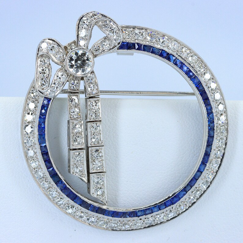 May include: A silver brooch with a diamond bow and a circle of sapphires and diamonds.