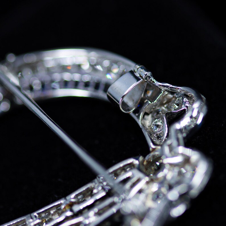 May include: A silver brooch with a crescent moon shape, set with sparkling diamonds. The brooch has a pin and catch closure.